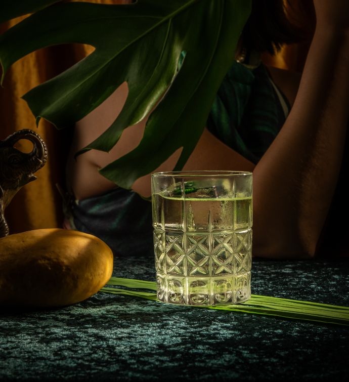 Light green cocktail in a short glass with palm leaf in the background