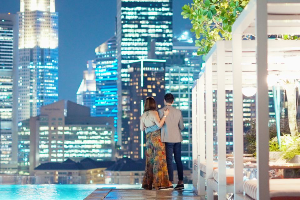 Image of a couple embracing each other on a rooftop by the pool, cabanas with a city skyline