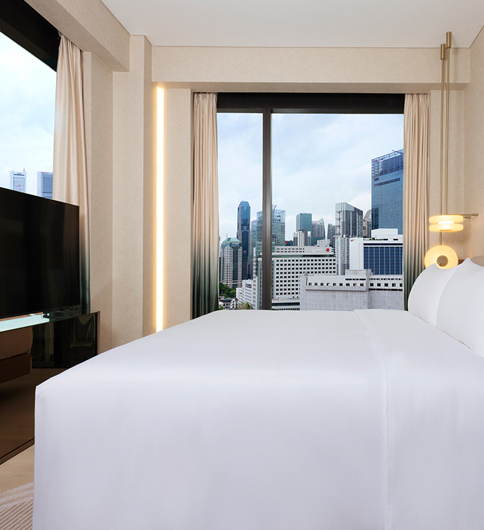 A hotel room with a bed, a TV, and a stunning city view from the window.