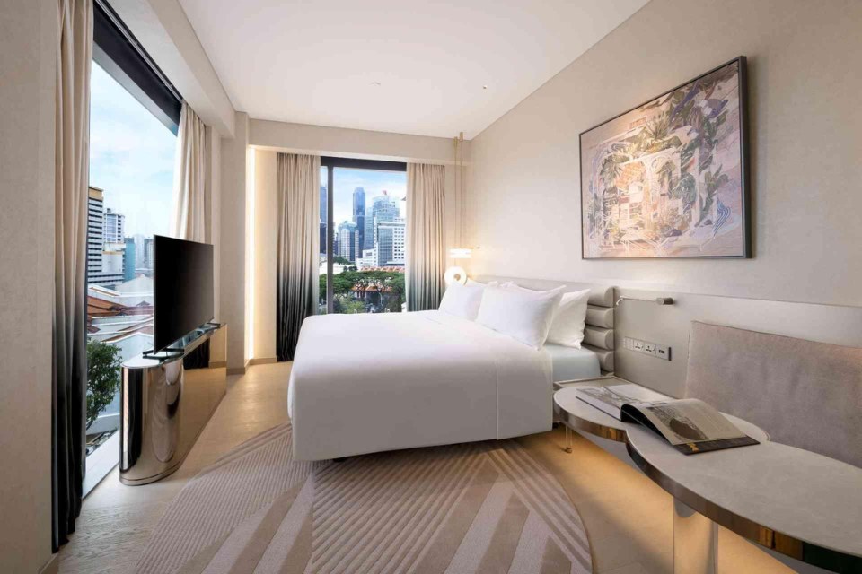 Bedroom at Mondrian Singapore with a large king bed, TV and windows with city views