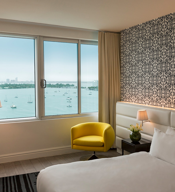 Habitación de hotel con una cama, una silla amarilla y una ventana con vistas al mar.