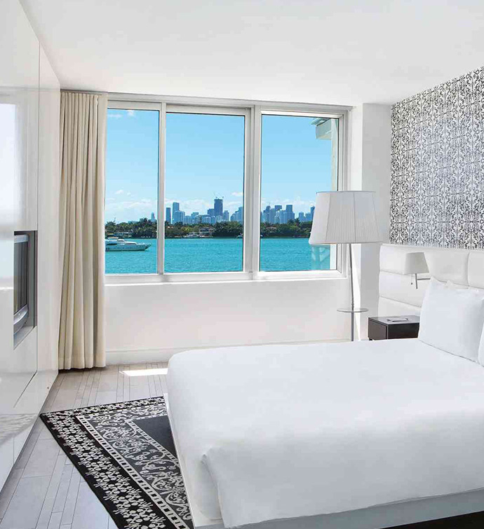 Habitación de hotel con cama, televisor y ventana con vistas al agua.