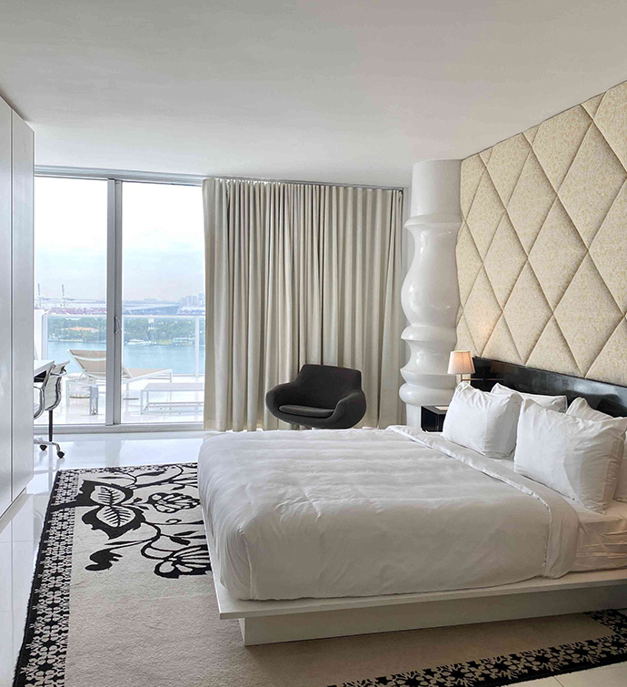 A cozy bedroom with a comfortable bed, a stylish chair, and a window with balcony with an ocean view.