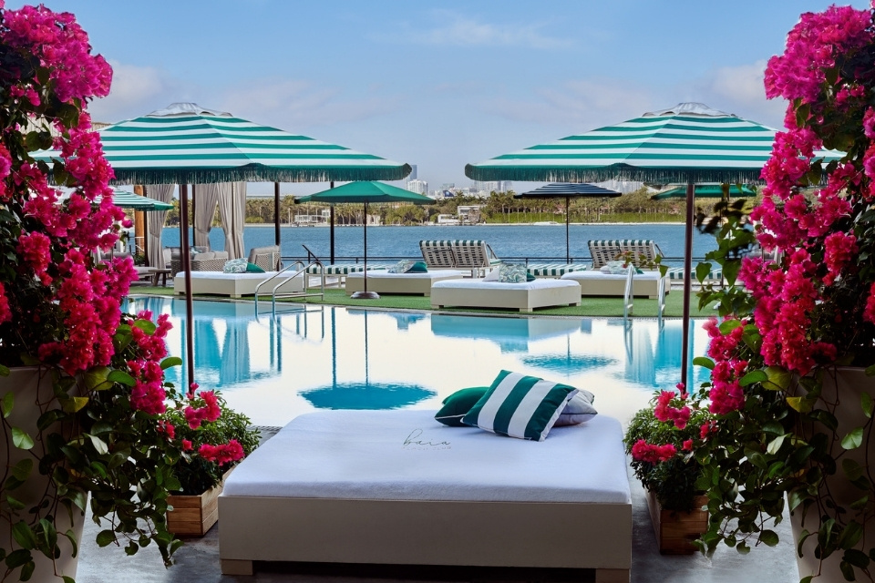 White chaise lounge framed with pink flowers with a pool and beach in the distance