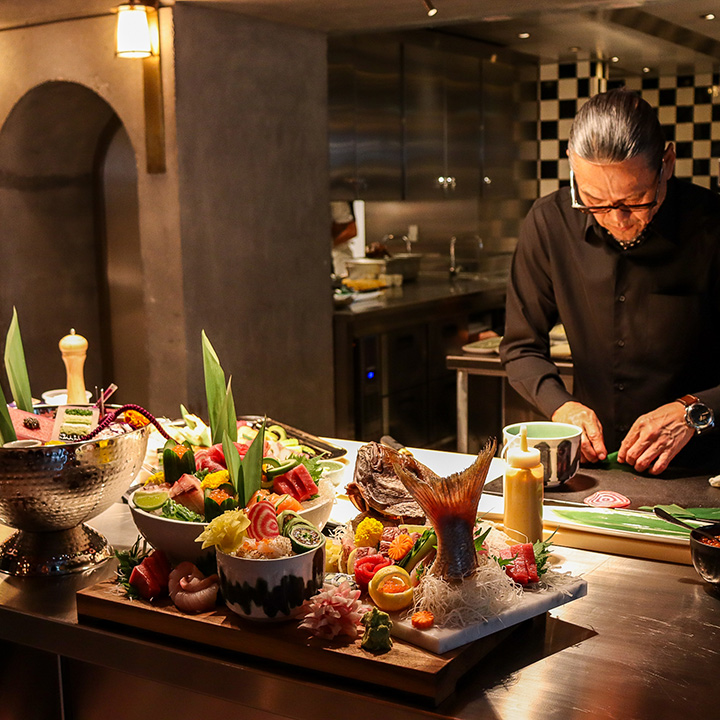 El chef Morimoto cocinando en una mesa con varios platos preparados en primer plano