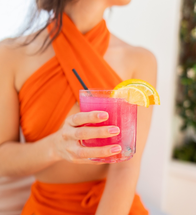 Mujer con un vestido halter naranja sosteniendo un cóctel rosa en Skybar Los Angeles