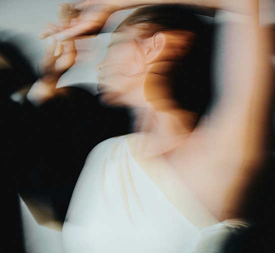 Image floue représentant une femme en robe blanche avec une épaule dénudée en train de danser.