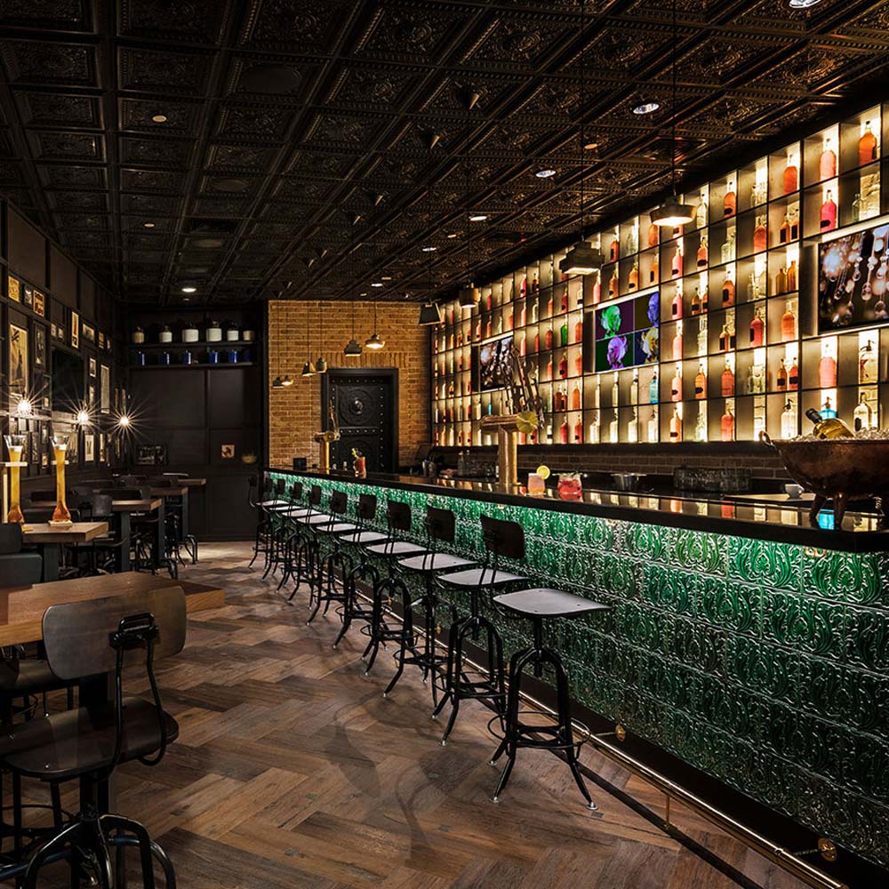 The Hudson Tavern bar with green bar, line of grey barstools, and brightly light back of the bar.