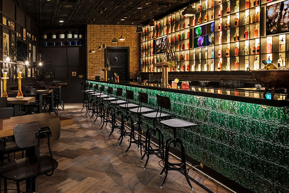 The Hudson Tavern bar with green bar, line of grey barstools, and brightly light back of the bar.