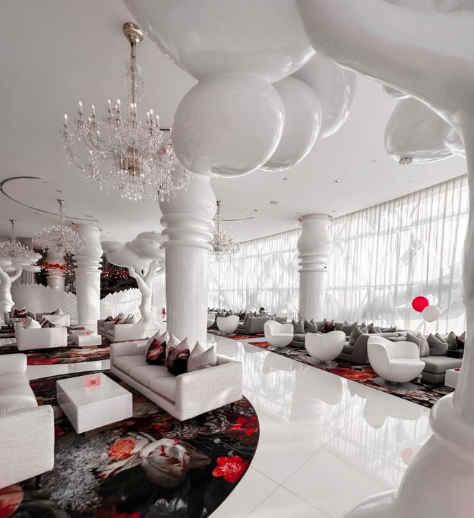 Interior del restaurante Ellamia Doha con modernos asientos blancos, lámparas de araña y pilares de gran tamaño