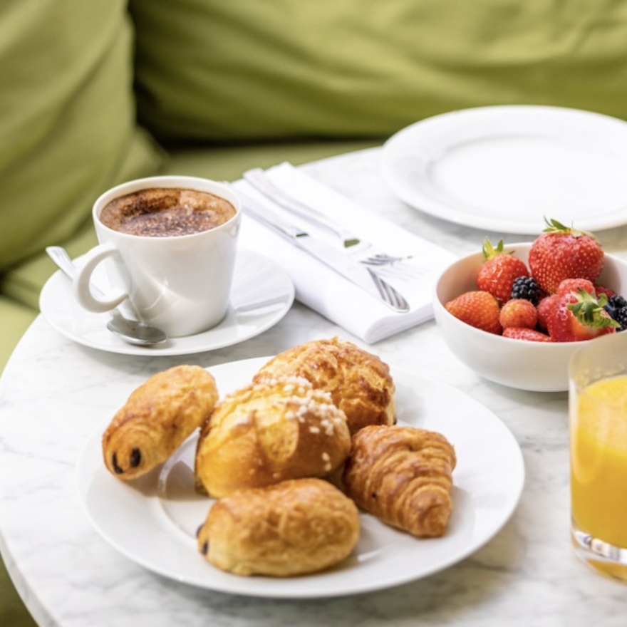 Table garnie avec un petit déjeuner comprenant du café, du jus de fruits, des viennoiseries et des fraises