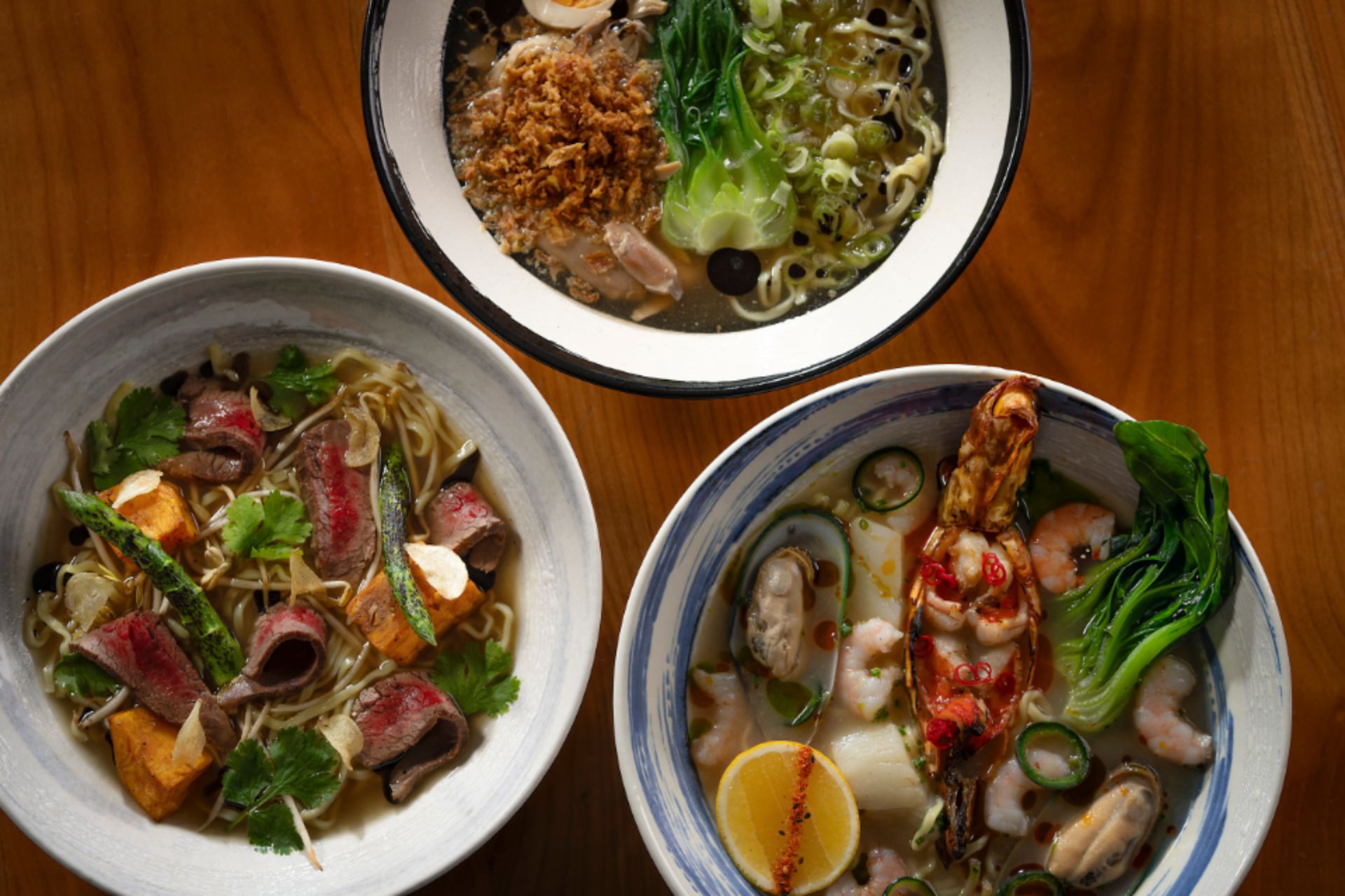 three bowls of distinct, colorful and delicious ramen on a wooden table.