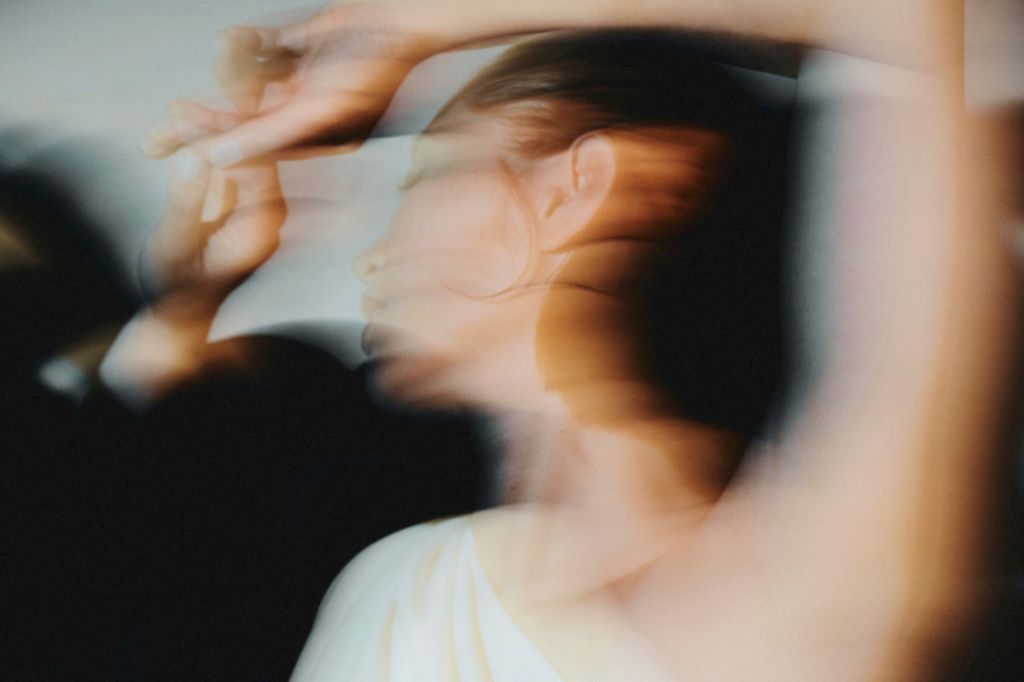 Image floue représentant une femme en robe blanche avec une épaule dénudée en train de danser.