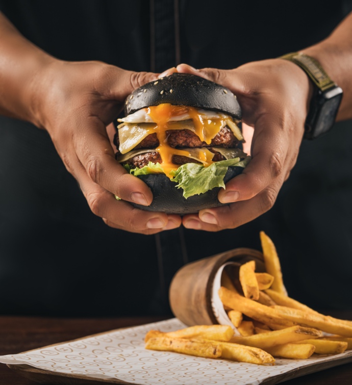 Hand holding a burger with fries below it