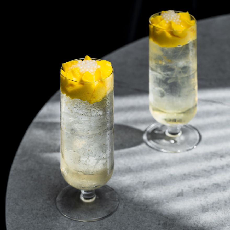 Two pina coladas with yellow garnishes in tall glasses sit on a grey table