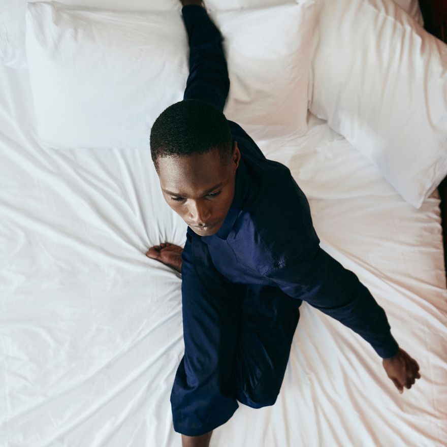 Man in dark pajamas poses abstractly on an all white bed