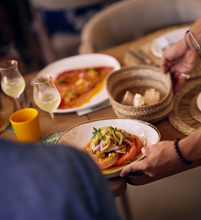 Plates of food being served on a table with other dishes and two glasses of white wine