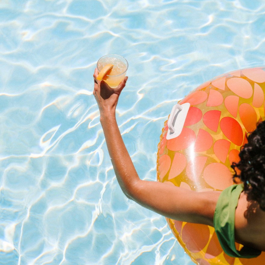 Mujer en un flotador de piscina sosteniendo un cóctel sobre la piscina