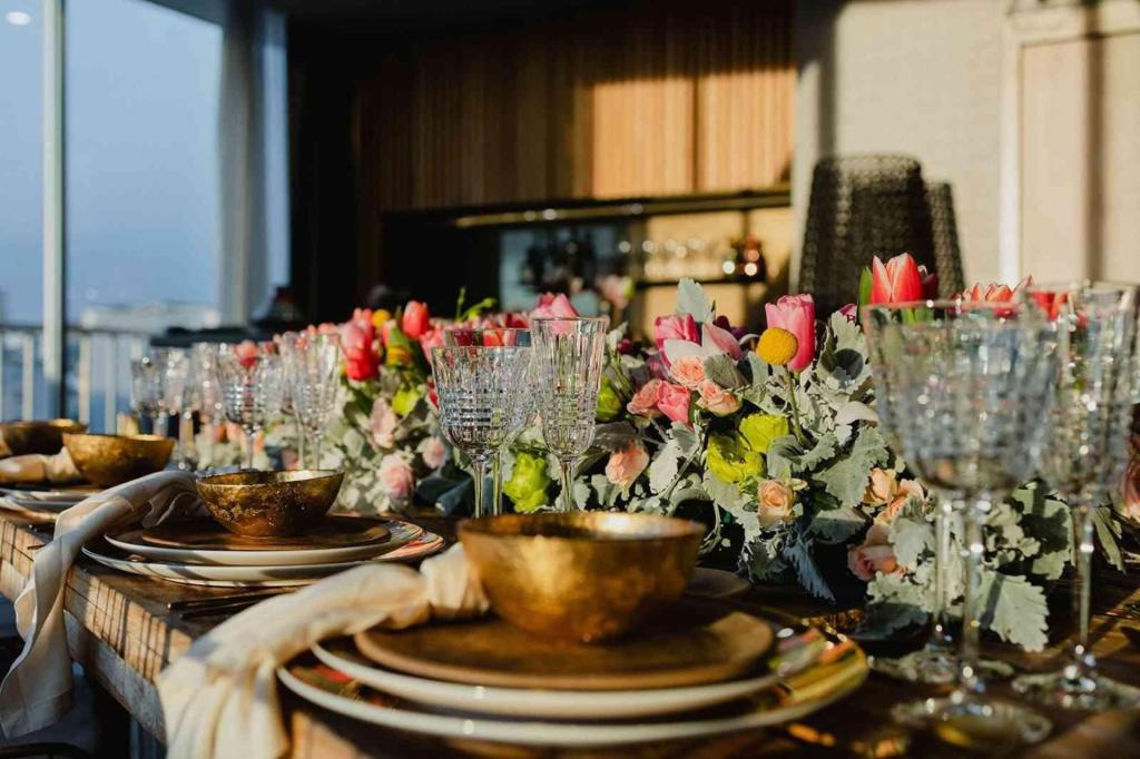 una preciosa mesa con platos y cuencos dorados, copas de cristal para champán y vino y tulipanes rosas.