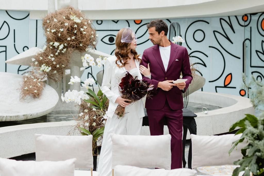 a bride and groom standing on a terrace with large floral arrangements behind them