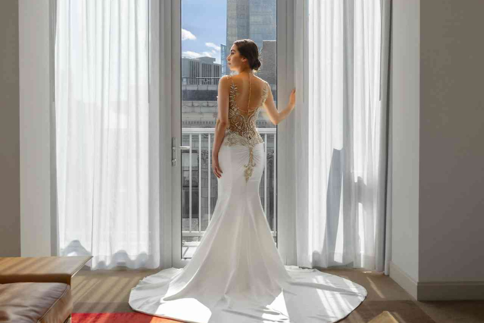 a beautiful bride in her wedding dress standing up against the window