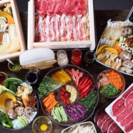 Table full of plates of raw vegetables and different cuts of raw meat