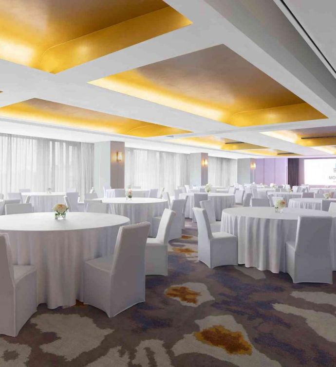 Ballroom with patterned colorful carpet and white round tables with white slipcovered chairs