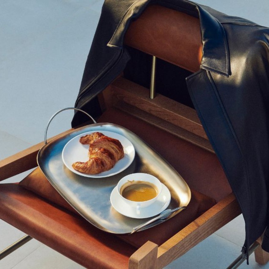 Un cruasán y un café sobre una silla de cuero marrón con una chaqueta de cuero negro colgando del respaldo