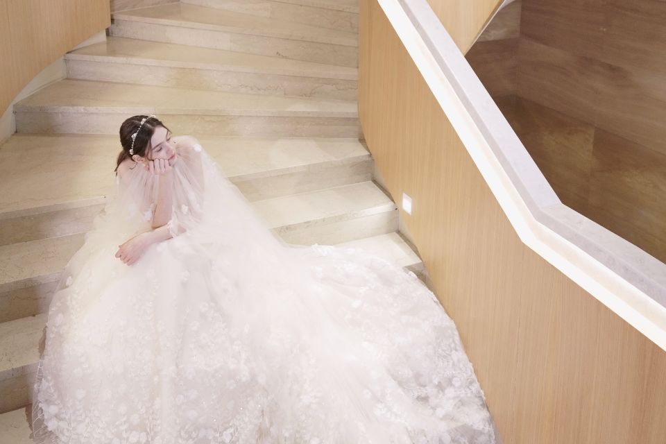 Bride in a white wedding dress sits on a large staircase and looks off into the distance