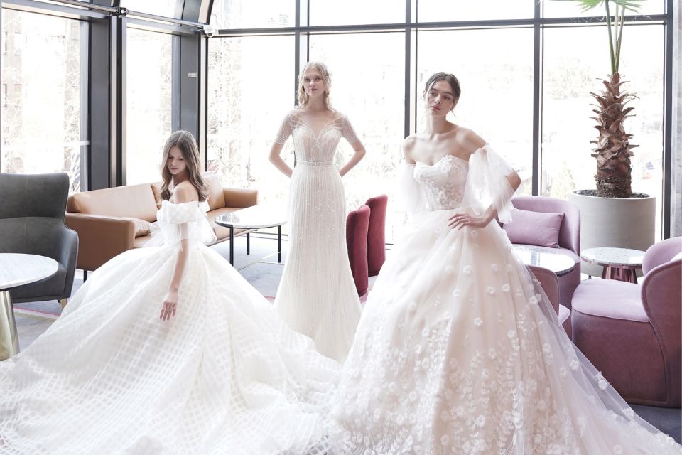 Three brides in wedding dresses stand in a lounge area with various sofas and chairs in the background