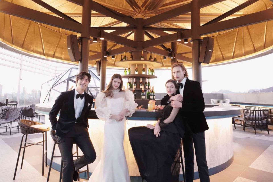 Bride in white gown, man in tux, woman in black dress and a man in tux with his arm around her all stand at a bar