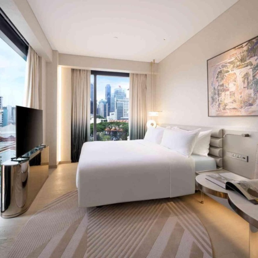 A spacious hotel room with a bed, a TV, a painting and a stunning city view from the window.