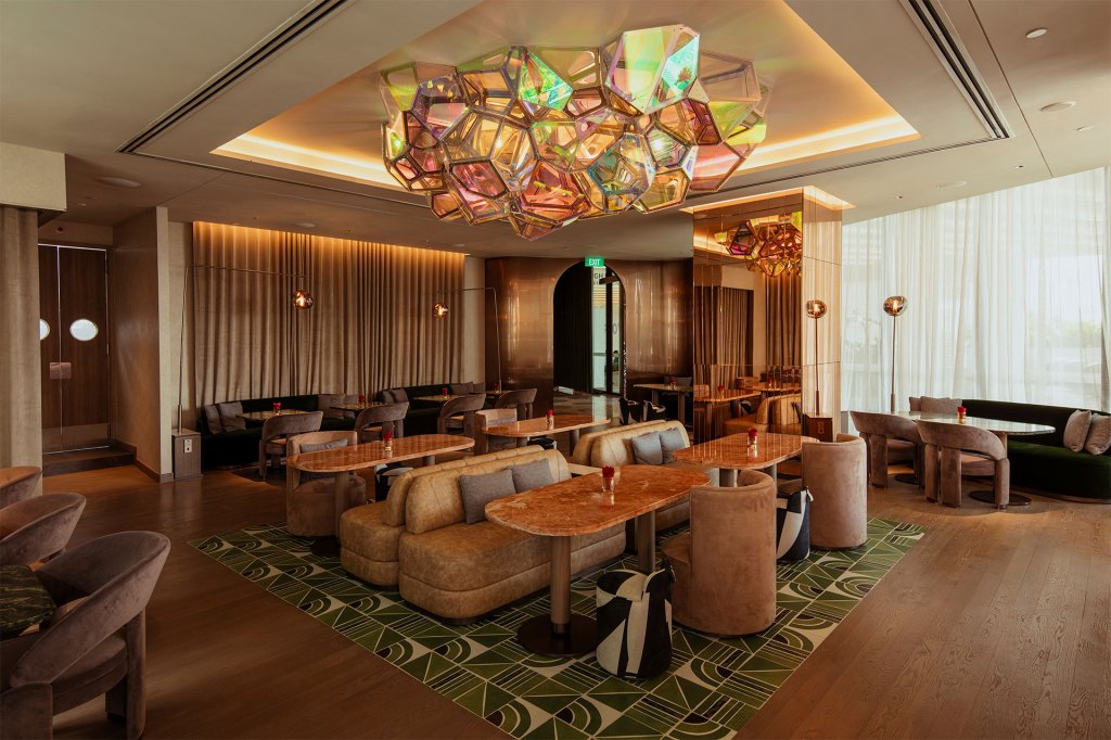 Lounge area with modern lighting piece, light brown booths, gold marble tables, and a green patterned carpet.