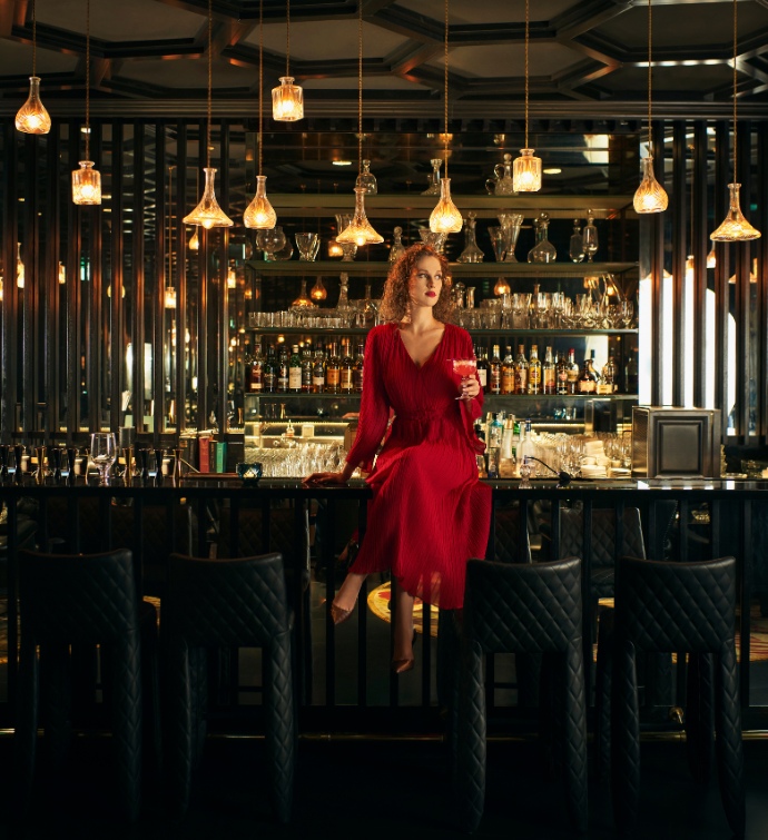 Femme en robe rouge assise à un bar buvant un cocktail