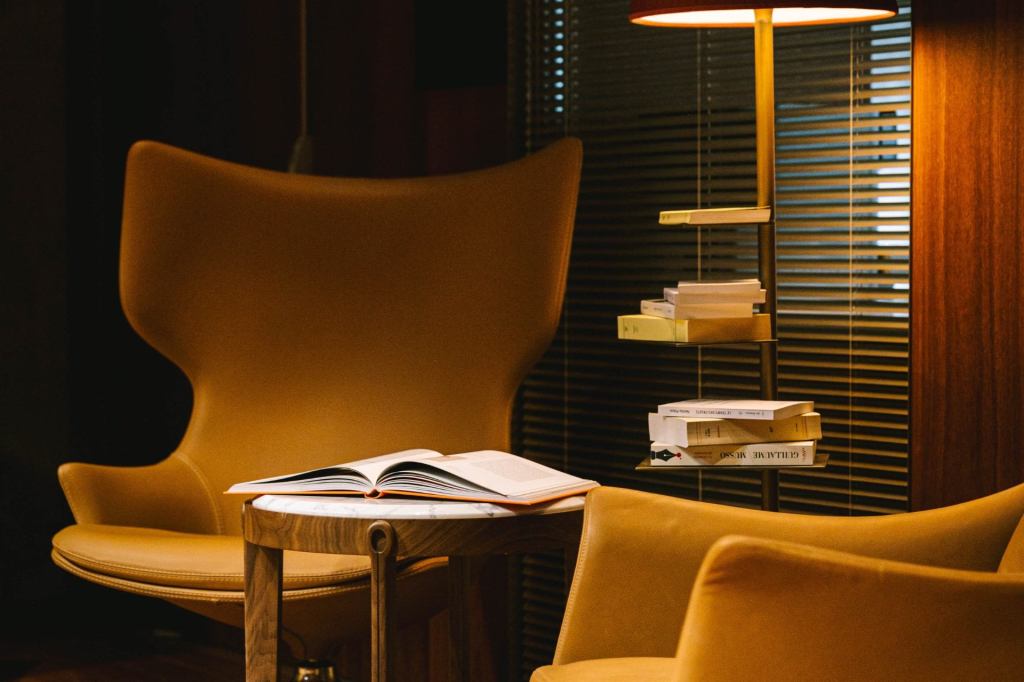 Two high-back armchairs upholstered in tan fabric alongside an accent table holding an open book