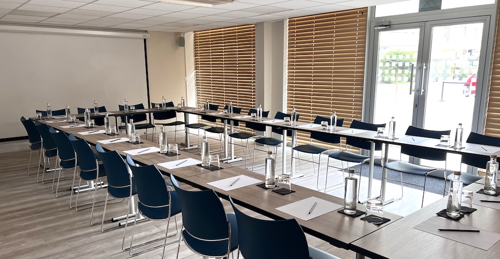 Large conference room with rectangular tables set up in a larger rectangular and chairs set up behind each table