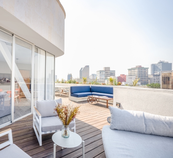 Large terrace with white and light grey sofa and chairs and a small white round table with plant on top and city in the skyline.