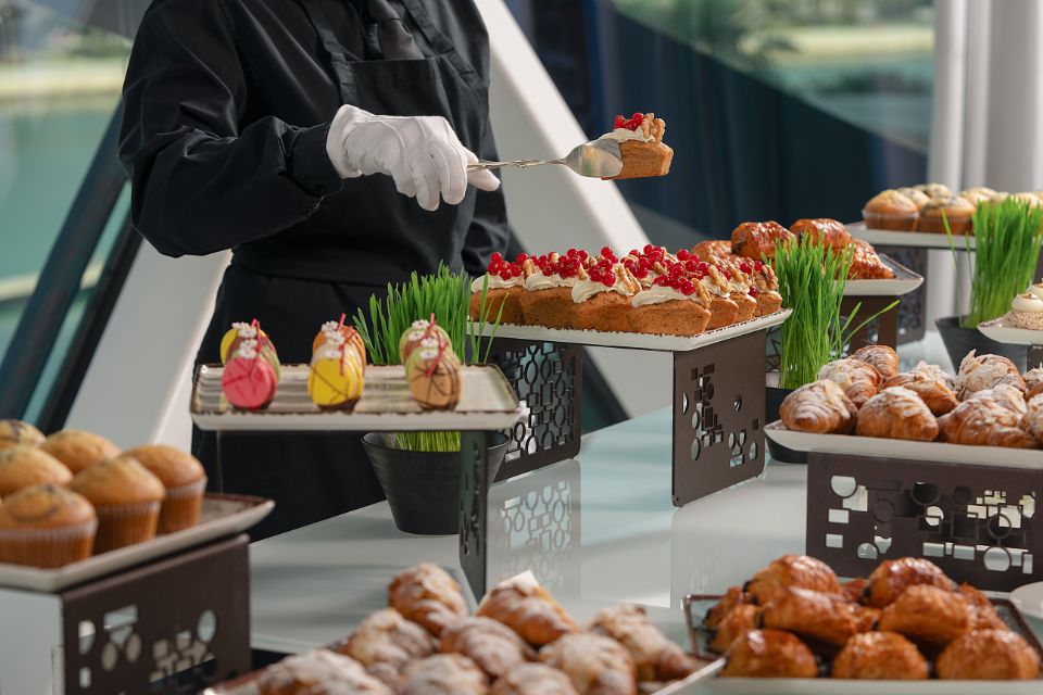 Buffet set up of pastries with person in all black and a gloved hand picking up a pastry with tongs