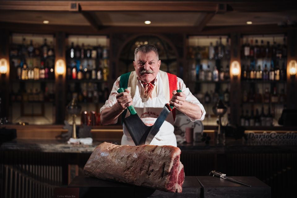 Butcher posing with knives in front of a hunk of meat