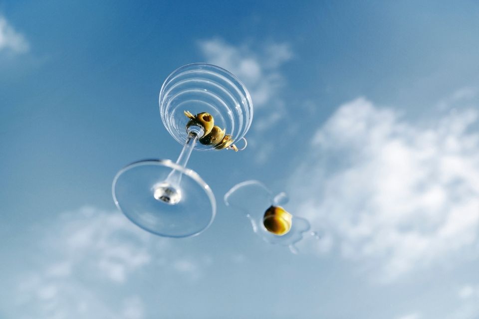 Preciosa copa de martini con aceitunas dentro y un cielo azul con nubes al fondo