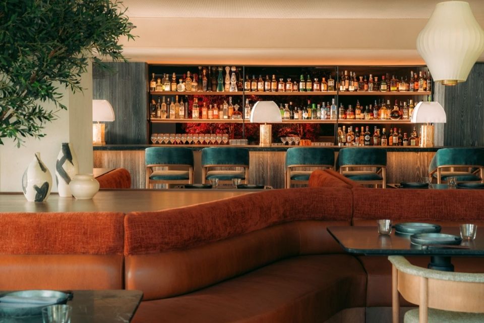 Rust colored dining booth with a modern wooden bar behind it and with teal barstools