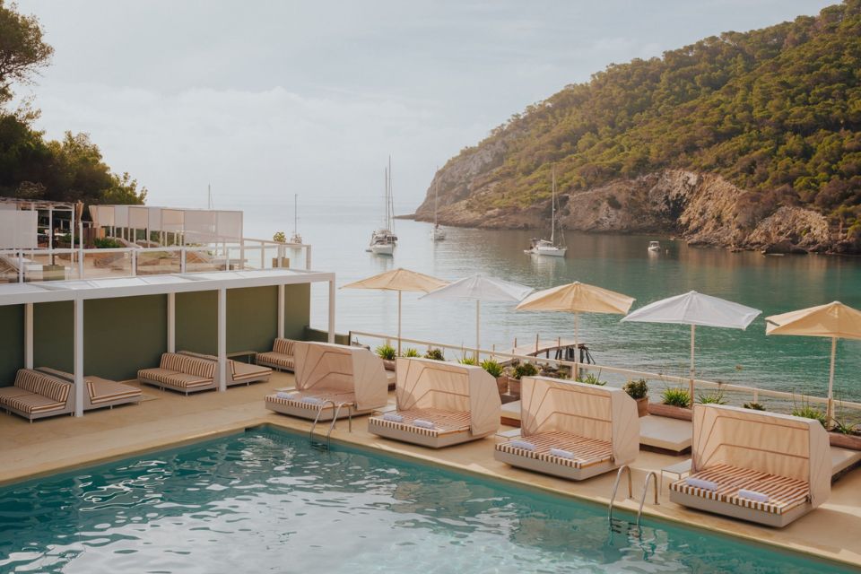 Large pool with covered cabanas and umbrellas with a sea and boats in the background