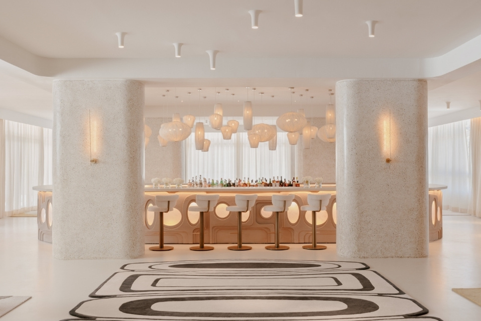 White bar with multiple white paper chandeliers and modern bar stools with black and white geometric patterned rug