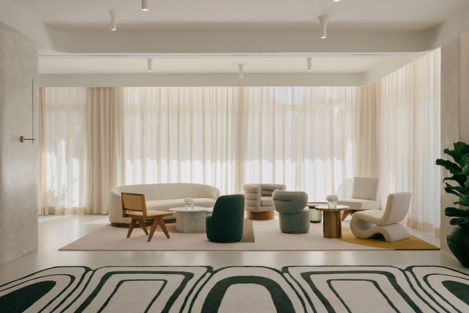 Large lobby space with black and white geometric rug, white sofa, modern chairs in various shapes and sizes, and a white curtain