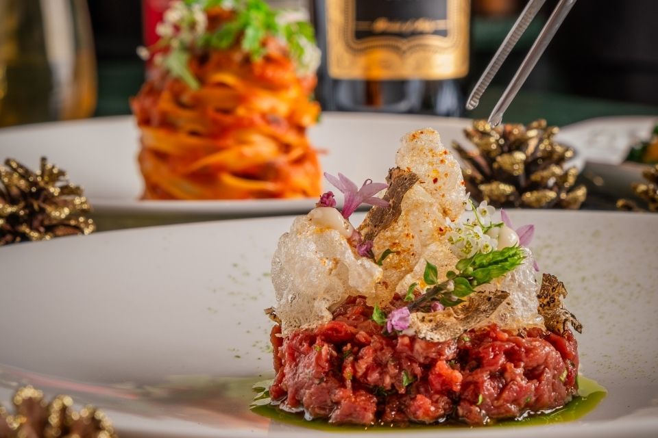 Beef tartare on a white plate with pasta on the plate behind it