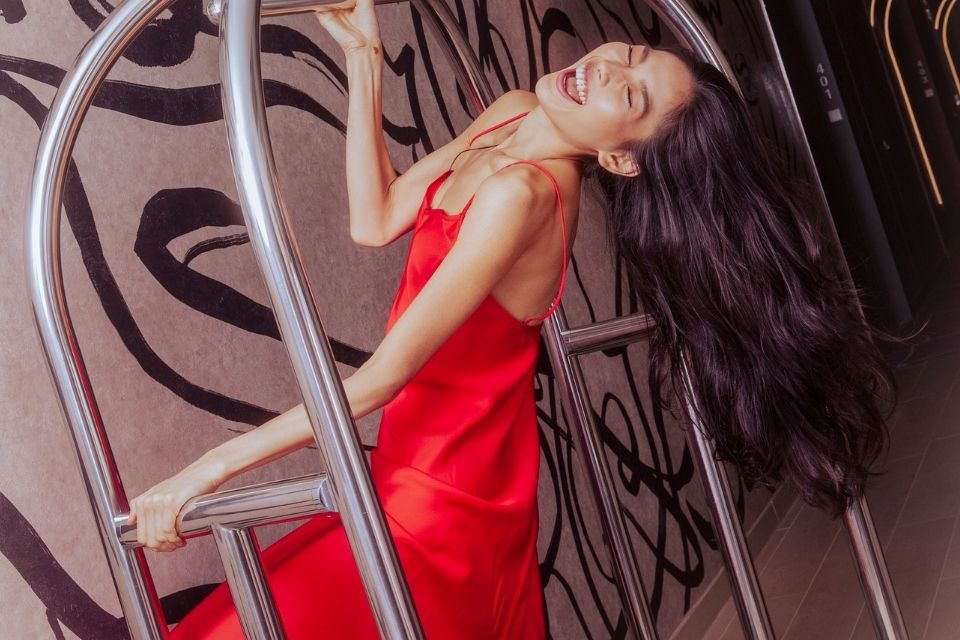 Woman in red dress laughs while on a luggage cart