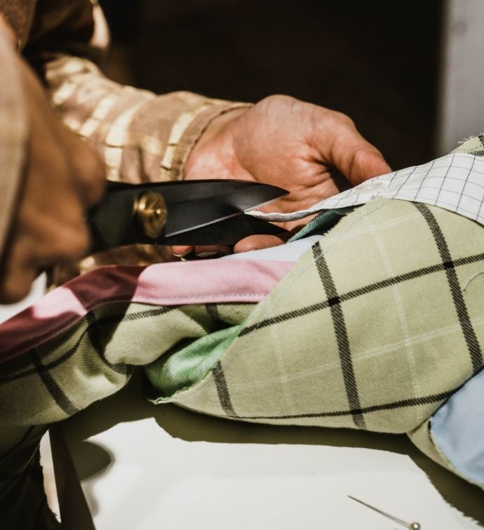 Close up image of plaid fabric with hands cutting it with scissors