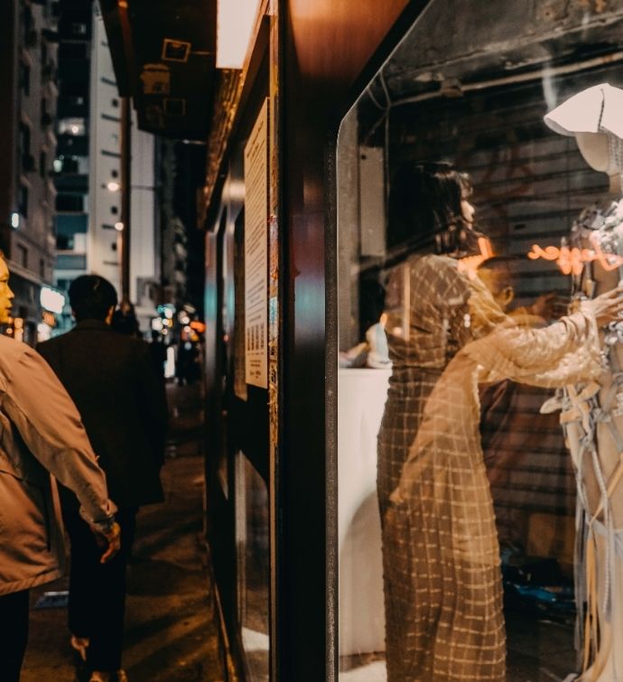 Woman dressing a mannequin in a window front shop with a man passing on the street nearby