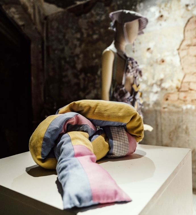 Textile based sculpture sits on a white table with a mannequin in the background