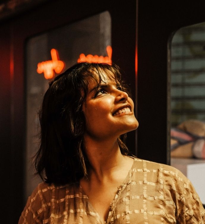 Woman with dark short hair and tan blouse smiles looking out of frame